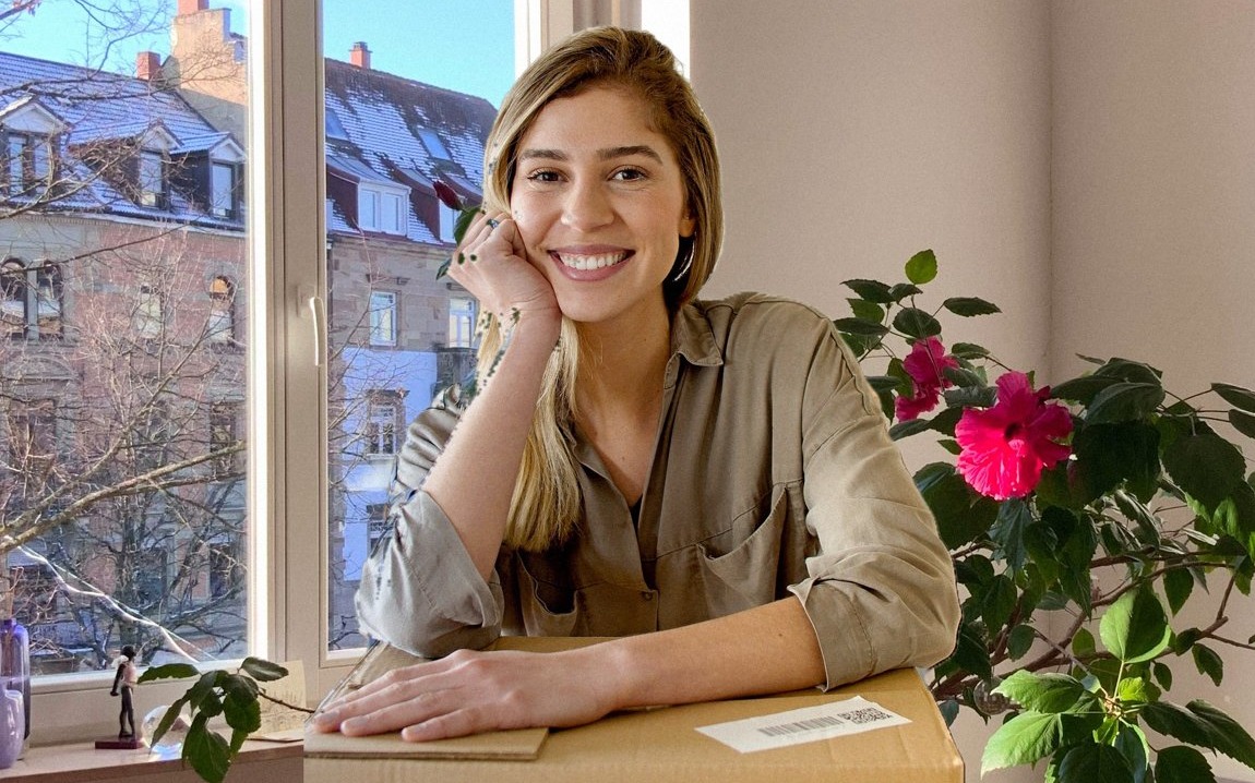 Zufriedene Kundin mit versandfertigem Paket, helles Wohnzimmer